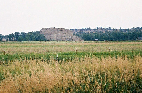 [A large stone sits in the grass by itself. It is the same height as the rock on the opposite side of the river, but that rock runs the length of the river at this location while the rock is the only thing at that height on this side of the river.]